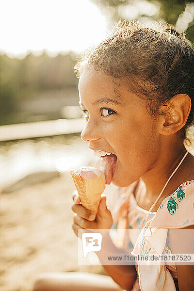 Mädchen schaut seitwärts  während sie an einem sonnigen Tag Eis leckt