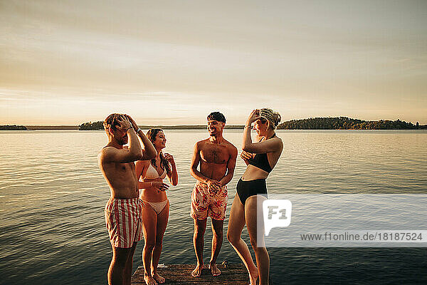 Glückliche junge Männer und Frauen  die sich auf einem Steg am See unterhalten  während sie im Urlaub sind