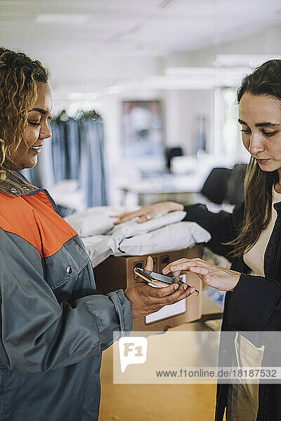 Lächelnde weibliche Lieferperson  die eine digitale Unterschrift von einem Modedesigner entgegennimmt  während sie ein Paket ausliefert