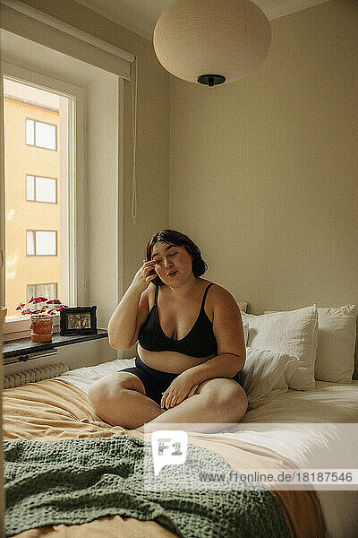 Young woman sitting cross-legged on bed at home