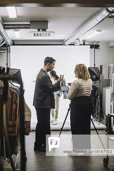 Side view of male fashion designer assisting photographer during photo shoot in studio