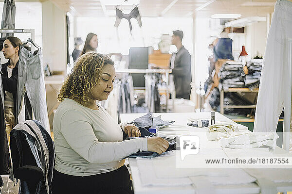 Seitenansicht einer jungen Modedesignerin  die bei der Arbeit im Atelier einen Stoff untersucht