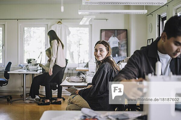 Porträt einer lächelnden Modedesignerin  die in einer Werkstatt sitzt