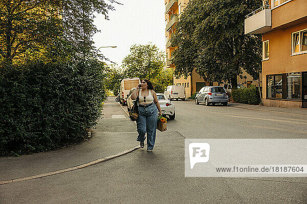 Junge Frau spricht in voller Länge mit ihrem Handy  während sie auf der Straße geht