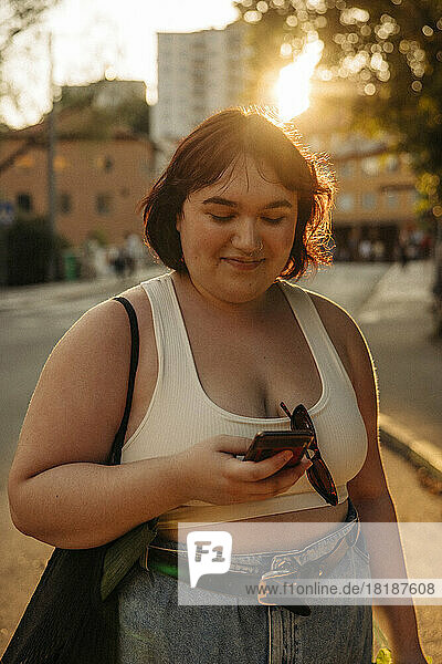 Lächelnde Frau  die bei Sonnenuntergang über ihr Smartphone im Internet surft