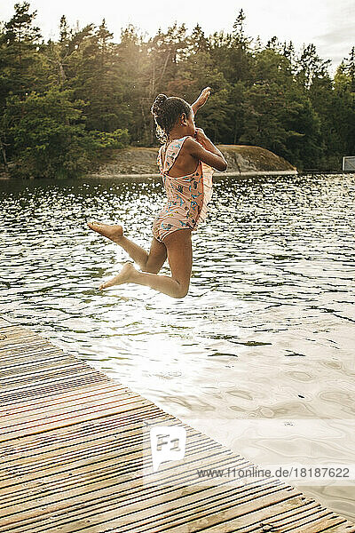 Unbekümmertes Mädchen  das im Urlaub vom Steg in den See springt