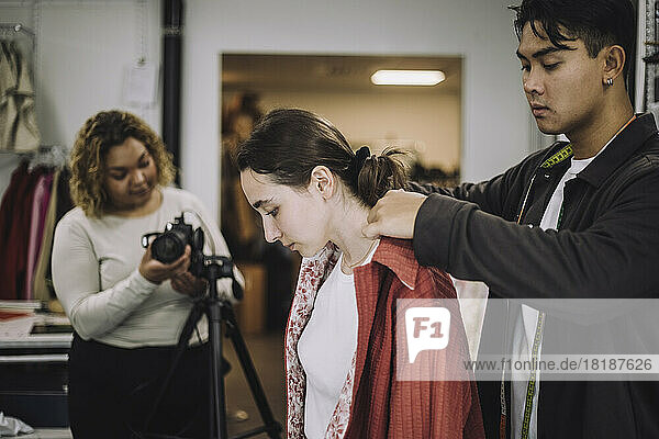 Männlicher Designer passt den Hemdkragen bei einem weiblichen Modell während eines Fotoshootings im Studio an