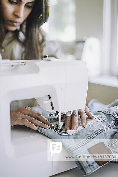Weibliche Modedesignerin näht mit einer Nähmaschine in einer Werkstatt Stoff auf eine Jeanstasche