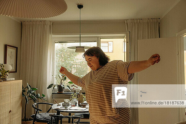 Smiling carefree young woman with arms outstretched dancing at home