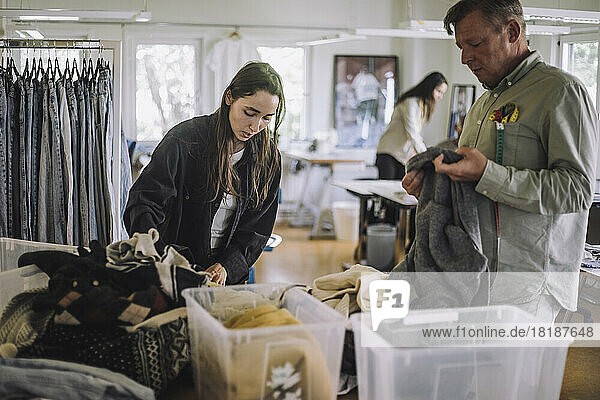Eine Modedesignerin und ein männlicher Kollege sortieren in einer Werkstatt recycelte Kleidung
