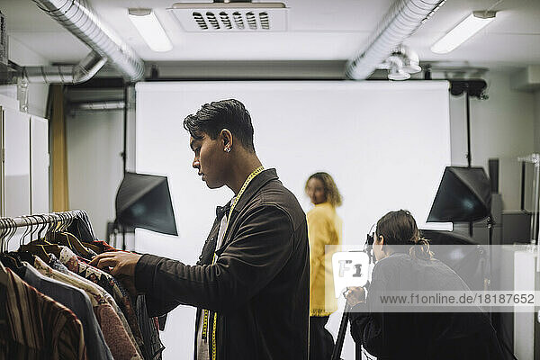 Seitenansicht einer Modedesignerin  die während eines Fotoshootings im Studio Kleider von der Stange auswählt