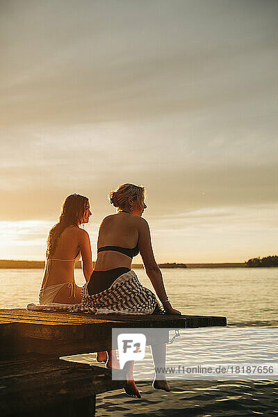 Frauen sitzen bei Sonnenuntergang auf einem Steg am See