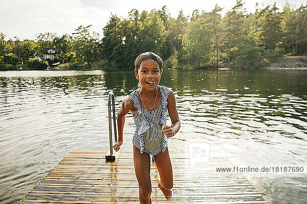 Porträt eines aufgeregten Mädchens  das nach dem Schwimmen im See auf den Steg läuft