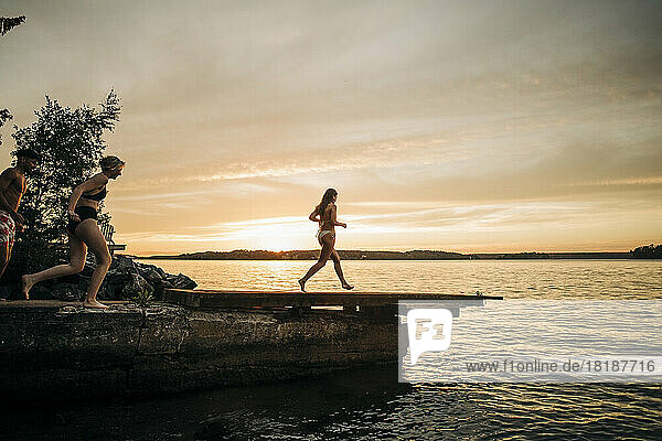 Freunde laufen im Urlaub bei Sonnenuntergang auf dem Steg Richtung See