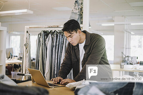 Concentrated male fashion designer using laptop at workshop