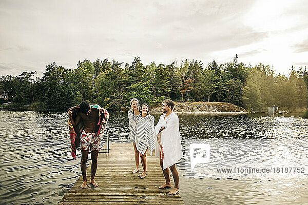 Glückliche Freunde  die ein Handtuch tragen  während sie im Urlaub auf dem Steg am See stehen