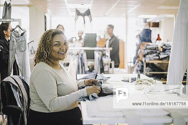 Portrait of smiling female fashion designer sitting at workbench in workshop
