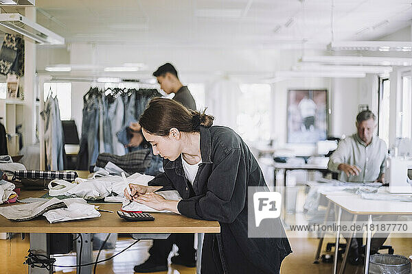 Junge Modedesignerin schreibt auf eine Verpackung  während sie in einer Werkstatt arbeitet