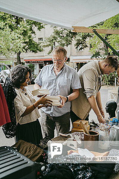Älterer männlicher Besitzer  der einer Kundin beim Kauf von Büchern auf dem Flohmarkt hilft