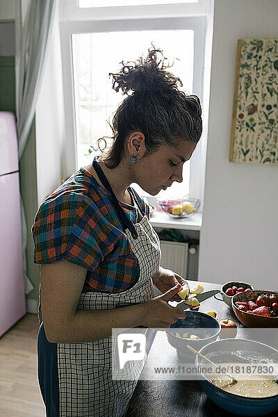 Frau mit Schürze schneidet Früchte bei der Zubereitung von Speisen in der Küche