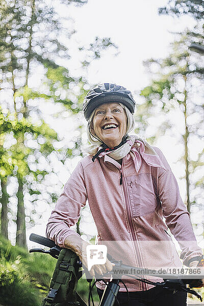 Lächelnde ältere Frau  die wegschaut  während sie mit dem Fahrrad steht