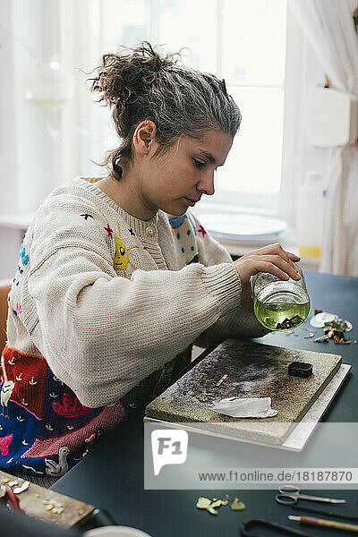 Weibliche Kunsthandwerkerin hält einen Krug  während sie zu Hause Schmuck herstellt