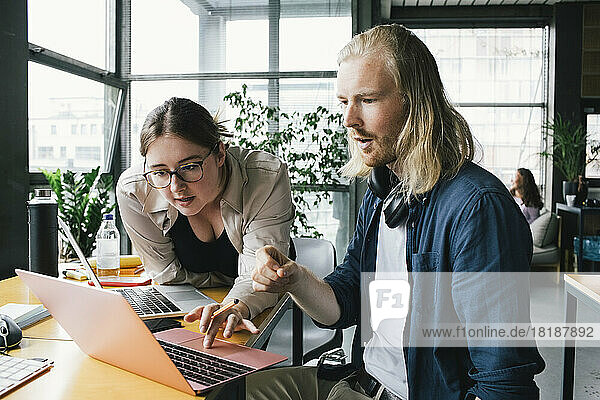 Eine Programmiererin bespricht mit einem männlichen Kollegen über einem Laptop in einem neuen Büro eine Strategie