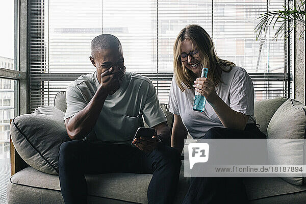 Cheerful male and female with drink bottle sitting on sofa during break time in office