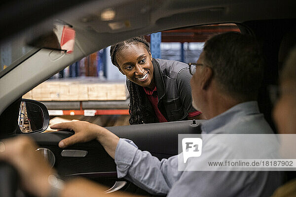 Lächelndes weibliches Verkaufspersonal betrachtet einen im Auto sitzenden Kunden in einem Baumarkt