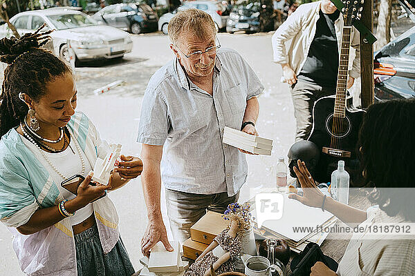 Blick von oben auf einen Kunden  der Bücher in der Hand hält  während er mit dem Besitzer auf dem Flohmarkt verhandelt