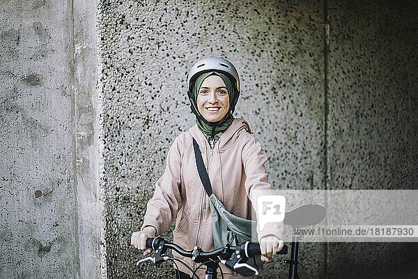 Porträt einer lächelnden jungen Frau mit Fahrrad  die in der Nähe einer Mauer steht