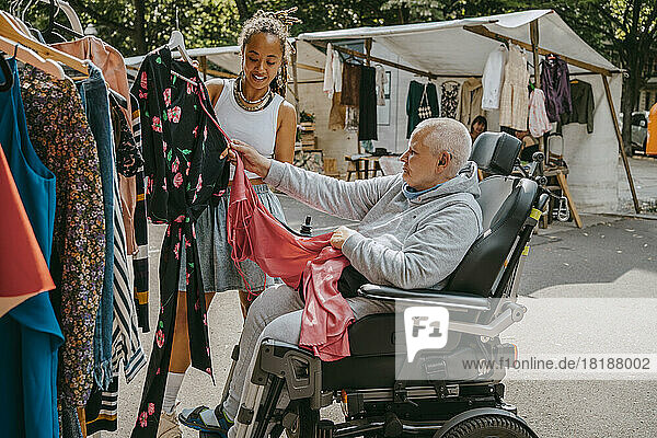Besitzerin hilft einer Kundin im Rollstuhl beim Kauf eines Kleides auf dem Flohmarkt