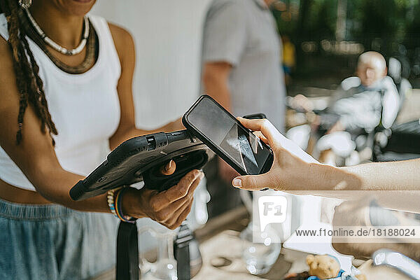 Hand of woman doing contactless payment while shopping at flea market