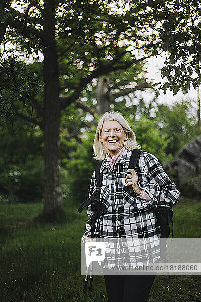 Porträt einer glücklichen älteren Frau mit Wanderstöcken beim Wandern im Wald