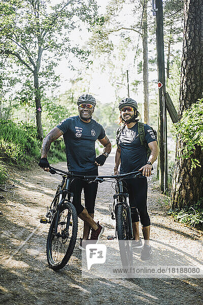Lächelnde männliche Freunde mit Fahrrädern auf dem Fußweg stehend