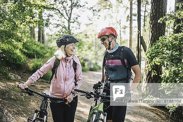 Happy male and female friends talking to each other holding cycles