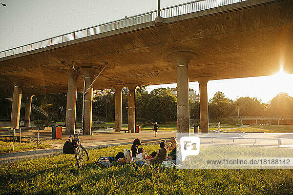 Teenager-Mädchen sitzen auf Gras bei der Brücke im Park bei Sonnenuntergang
