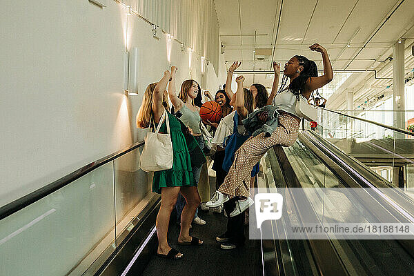 Teenager-Mädchen mit erhobener Hand genießt auf Rolltreppe in Einkaufszentrum