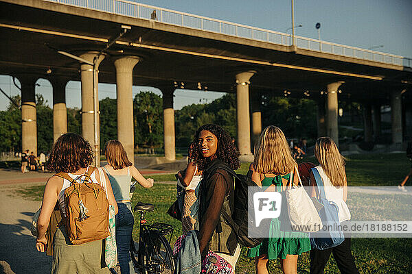 Porträt eines lächelnden Mädchens im Teenageralter  das mit Freunden gegen eine Brücke im Park läuft