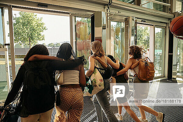 Rear view of teenage girls with arms around leaving shopping mall