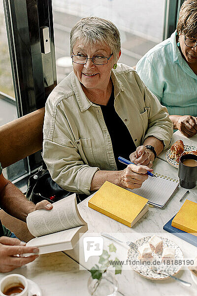 Hohe Winkel Ansicht der lächelnden älteren Frau mit Stift und Tagebuch sitzen von weiblichen Freund im Café