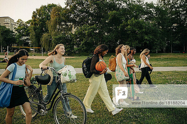 Lächelnde Teenager-Mädchen spazieren zusammen im Park bei Sonnenuntergang
