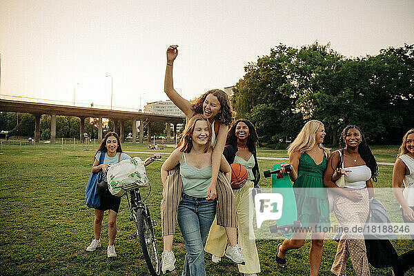 Happy teenage girl giving piggyback ride to female friend at park