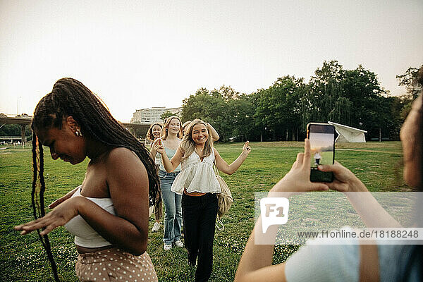 Teenager-Mädchen fotografiert Freundinnen  die im Park bei Sonnenuntergang tanzen
