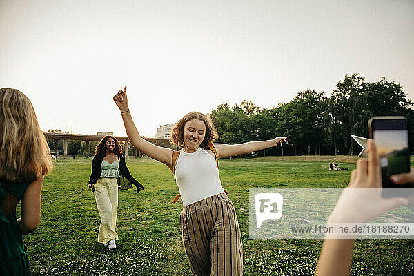 Teenager-Mädchen fotografiert sorglose Freundin tanzen im Park bei Sonnenuntergang