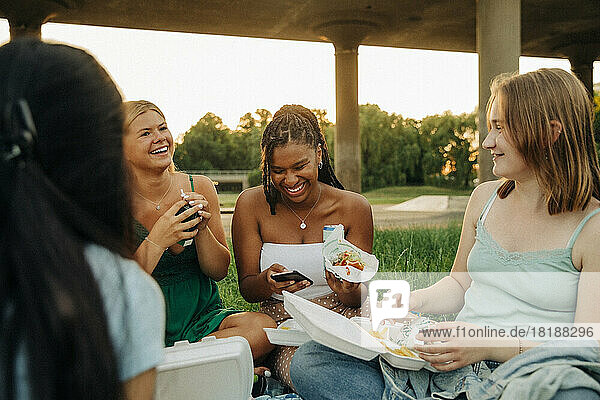 Glückliche Mädchen im Teenageralter unterhalten sich beim Essen im Park