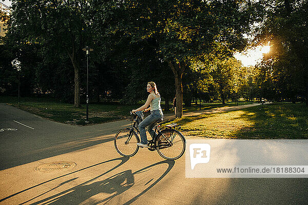 Seitenansicht von Teenager-Mädchen fahren Fahrrad auf der Straße im Park bei Sonnenuntergang