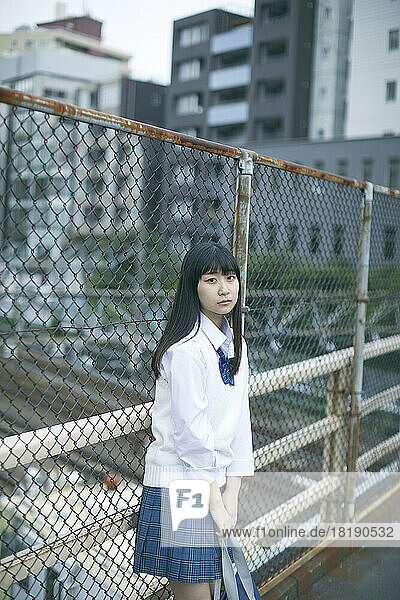 Japanese female high school student leaning against the fence