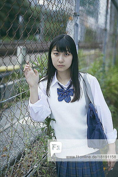 Japanese female high school student leaning against the fence