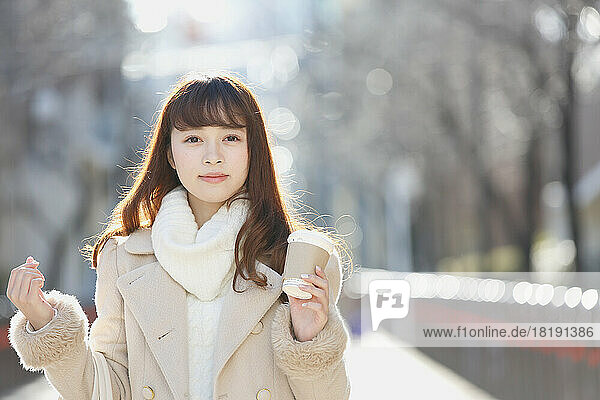 Japanese woman walking in town with coffee in one hand during winter